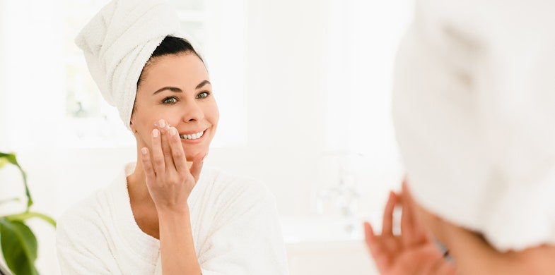 women putting cream on in the mirror